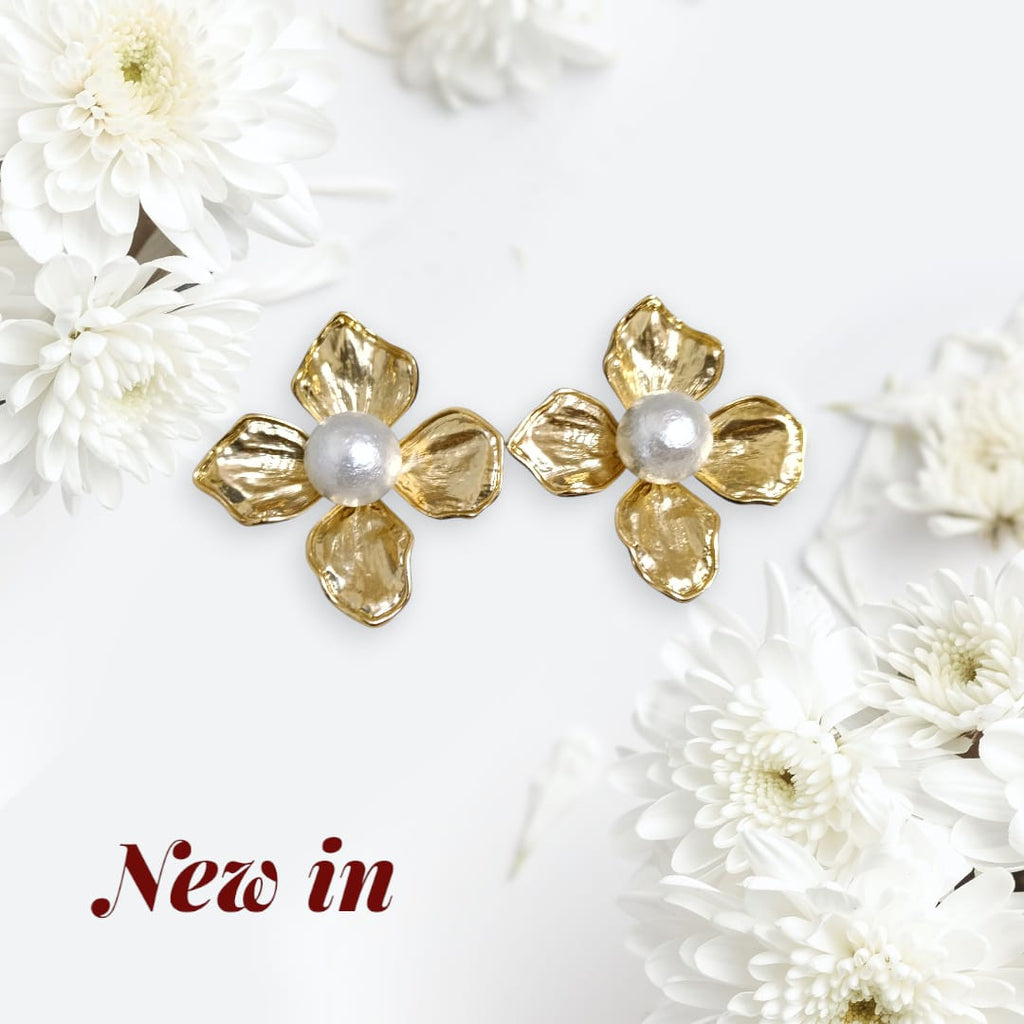 A pair of gold flower-shaped stud earrings with white pearl centers, displayed on a white background with decorative white flowers and the text 'New in' in the lower left corner.