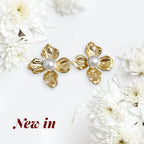 A pair of gold flower-shaped stud earrings with white pearl centers, displayed on a white background with decorative white flowers and the text 'New in' in the lower left corner.