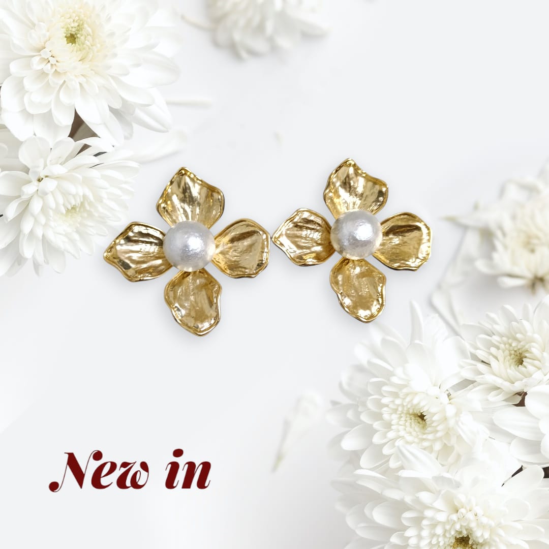 A pair of gold flower-shaped stud earrings with white pearl centers, displayed on a white background with decorative white flowers and the text 'New in' in the lower left corner.
