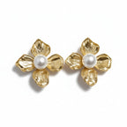 A pair of gold flower-shaped stud earrings with textured petals and a central white pearl, shown on a clean white background.