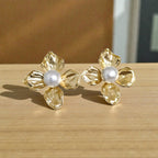 A pair of gold flower-shaped stud earrings with white pearl centers, resting on a light wood surface.