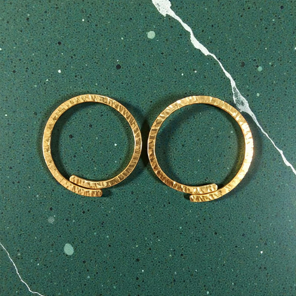 A pair of gold-toned textured hoop earrings displayed on a dark green speckled marble surface.