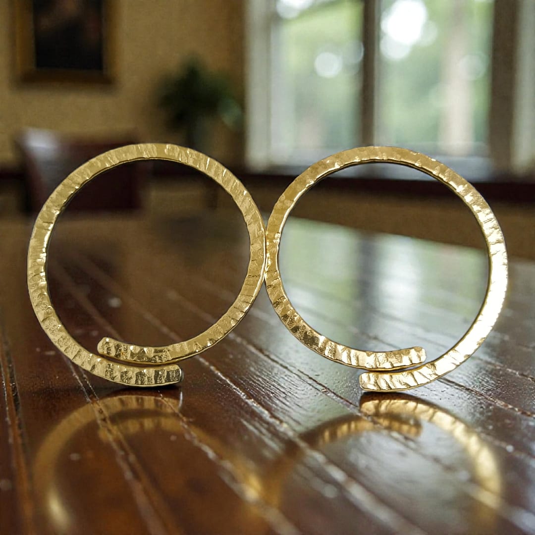 A pair of hammered gold hoop earrings displayed on a polished wooden table with a blurred indoor background.