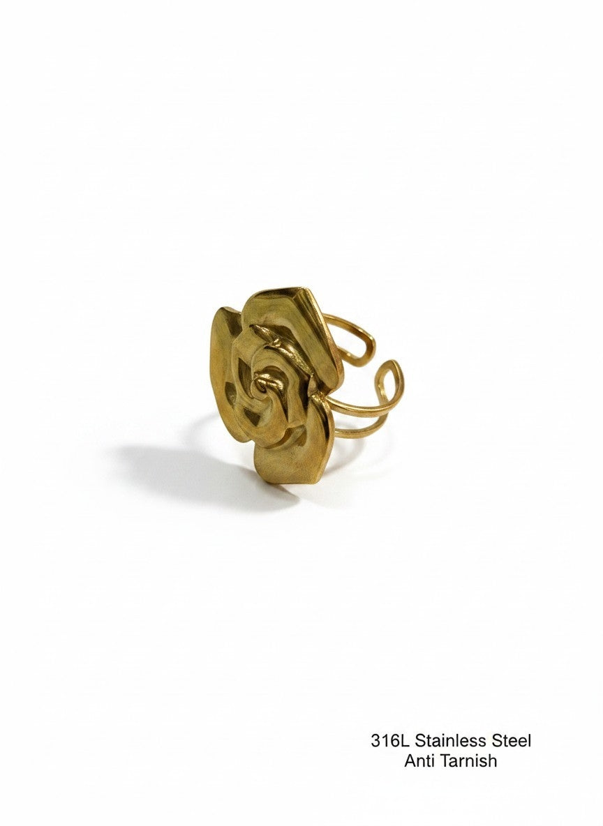 A gold-colored stainless steel ring with a sculptural, abstract flower-like top and a thin wire band, shown on a plain white background with a small text overlay in the bottom right corner.
Grishita Jewellery
