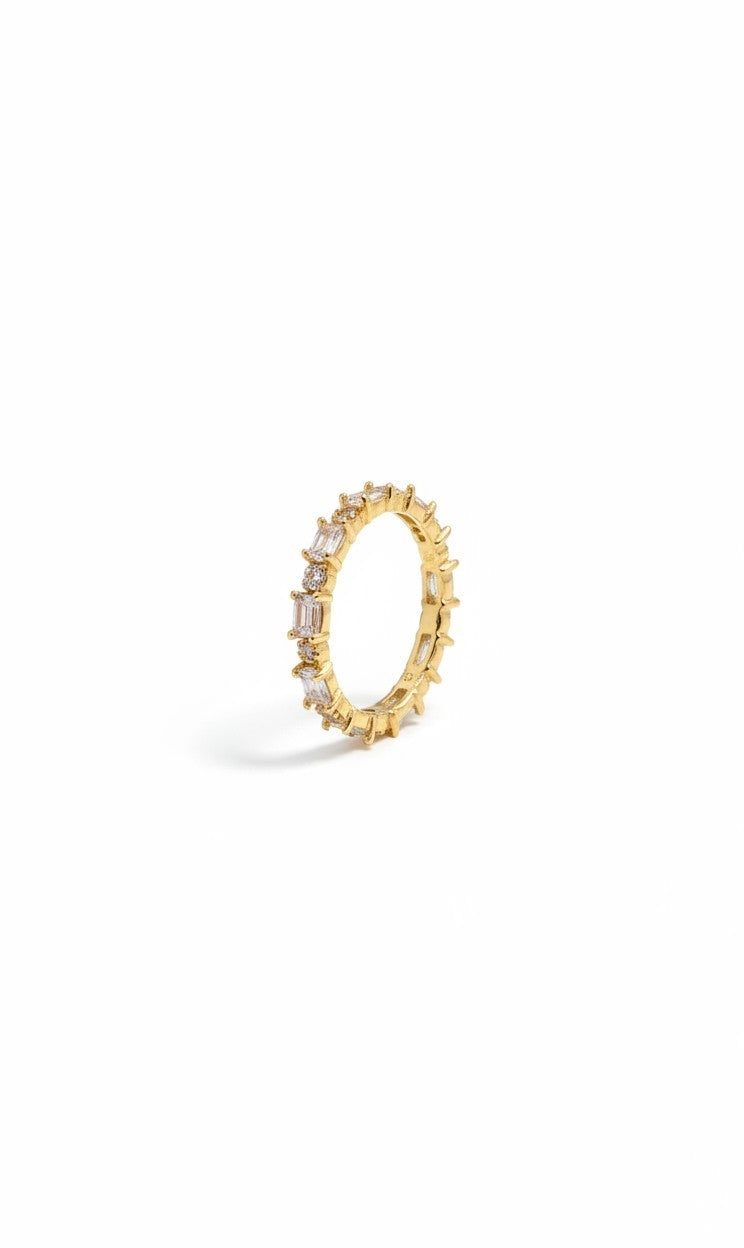 A gold eternity ring featuring baguette-cut clear stones set along the band, photographed on a clean white background with a soft shadow.
Grishita Jewellery
