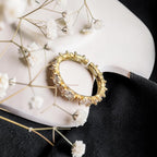 A gold ring with clear rectangular gemstones, styled on a white curved surface with white baby's breath flowers and a black fabric background.
Grishita Jewellery