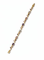 A delicate yellow gold bracelet featuring a vine-like design set with small pink, purple, and clear gemstones, shown on a plain white background.
Grishita Jewellery