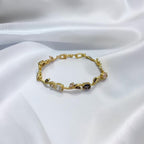 A delicate gold bracelet with small floral and geometric motifs, accented by clear and dark gemstones, displayed on a draped white satin fabric.
Grishita Jewellery