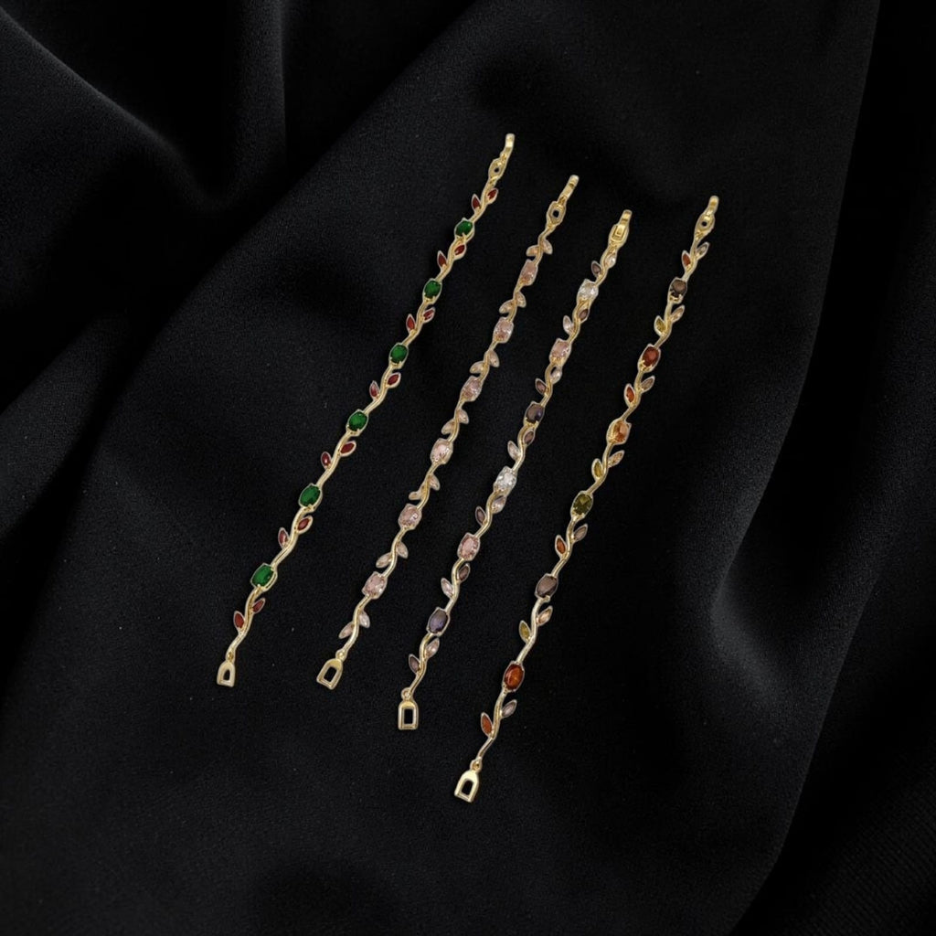 Four delicate gold-toned chain strands with small multicolored gemstone accents, arranged diagonally on a draped black fabric background.
Grishita Jewellery