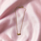 A delicate gold chain necklace with a small rectangular gold pendant engraved with the number '1111', displayed on a soft, draped pink satin fabric background.
Grishita Jewellery