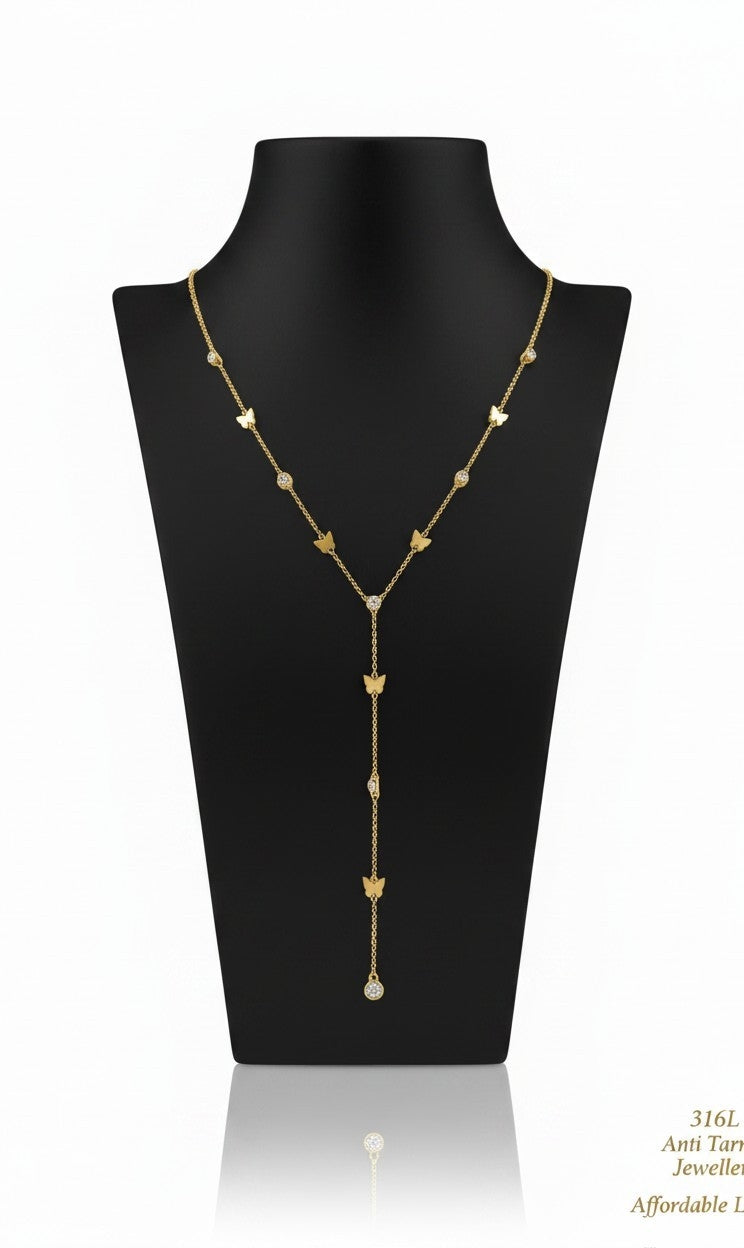 A gold lariat-style necklace with small butterfly motifs and a central drop ending in a pearl-like bead, displayed on a black jewelry bust against a white background.
Grishita Jewellery